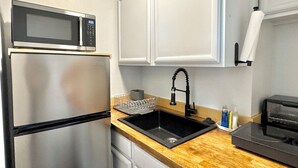 Una cocina compacta con un refrigerador de acero inoxidable, un microondas, un lavamanos con un grifo moderno y un tostador.