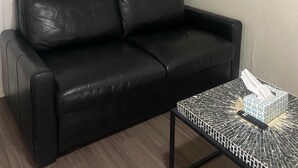Ein schwarzes Ledersofa, ein kleiner Tisch mit gemusterten Oberfläche und ein Elefantenbild an der Wand.