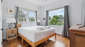 A bedroom with a wooden bed, two bedside tables, a ceiling fan, and large windows with curtains.