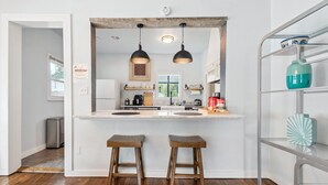 A kitchen with a central island, two bar stools, pendant lighting, and a metal shelving unit.