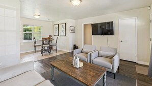En stue med sofa, sofabord, tv ophængt på væggen og et spiseområde med stole og bord.