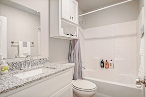 A bathroom with a white sink, mirror, and toilet. There is a shower with a curtain and toiletries on the wall. - 5BR Bethany home near Wiley Post & SNU. Hot tub, full kitchen. Sleeps 10. #COL (Oklahoma)