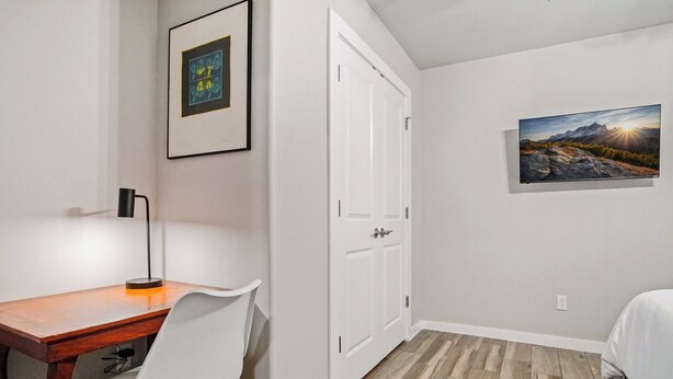 Une chambre à coucher avec un lit, un bureau avec une chaise, une porte et un tableau encadré au mur.