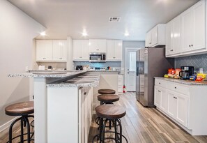 A modern kitchen with white cabinets, a granite countertop, and a built-in island with stools. - 5BR Bethany home near Wiley Post & SNU. Hot tub, full kitchen. Sleeps 10. #COL (Oklahoma)