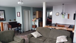 A living room with a sofa, armchair, and a dining table. There is a piano and a kitchen in the background. - Cozy Apartment in the Heart of Downtown Geneva (Geneva)