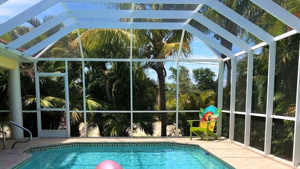 Zwembadgedeelte met glazen omheining, een roze flamingo drijvend object en een stoel met tropisch ontwerp.