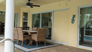 Un espace patio extérieur avec une table et des chaises, un ventilateur de plafond et une porte-fenêtre coulissante.