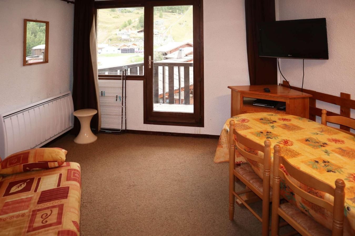 A hotel room with a bed, a small table, a television, and a window with a view of buildings.