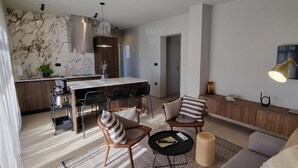 Eine moderne Küche mit Marmorfliesenspiegel, ein Essbereich mit Holztisch und Stühlen sowie ein Wohnbereich mit Sofa und Couchtisch.