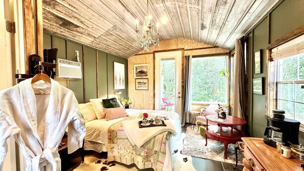 Ein gemütliches Schlafzimmer mit einem Bett, einer Holzkommode, einer Kaffeemaschine und einem Fenster mit Vorhängen.