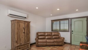 A room with a wooden cabinet, a leather sofa, a window with blinds, and a green door.