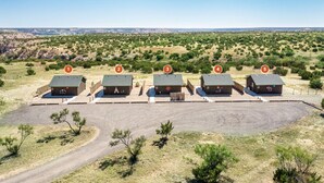 A row of five cabins with numbered signs, surrounded by a dry landscape and sparse vegetation.