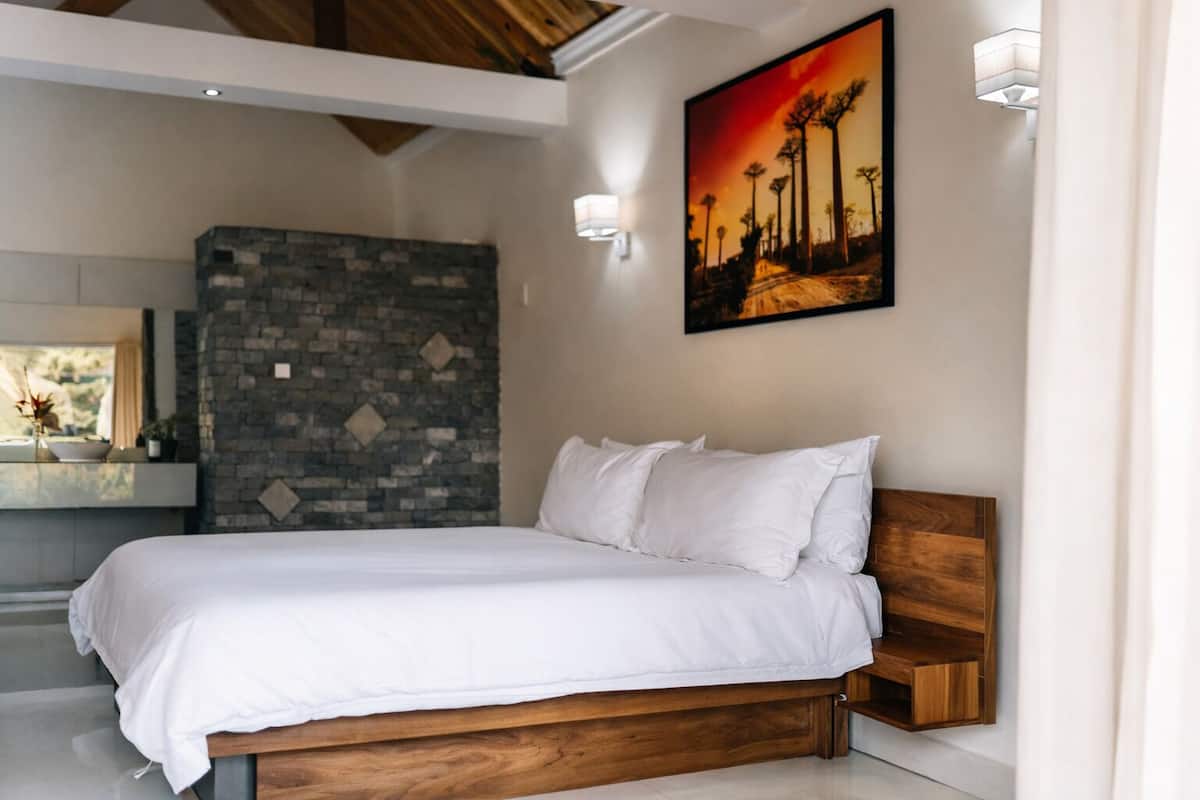 A bedroom with a wooden bed, a stone wall, and a sunset painting.