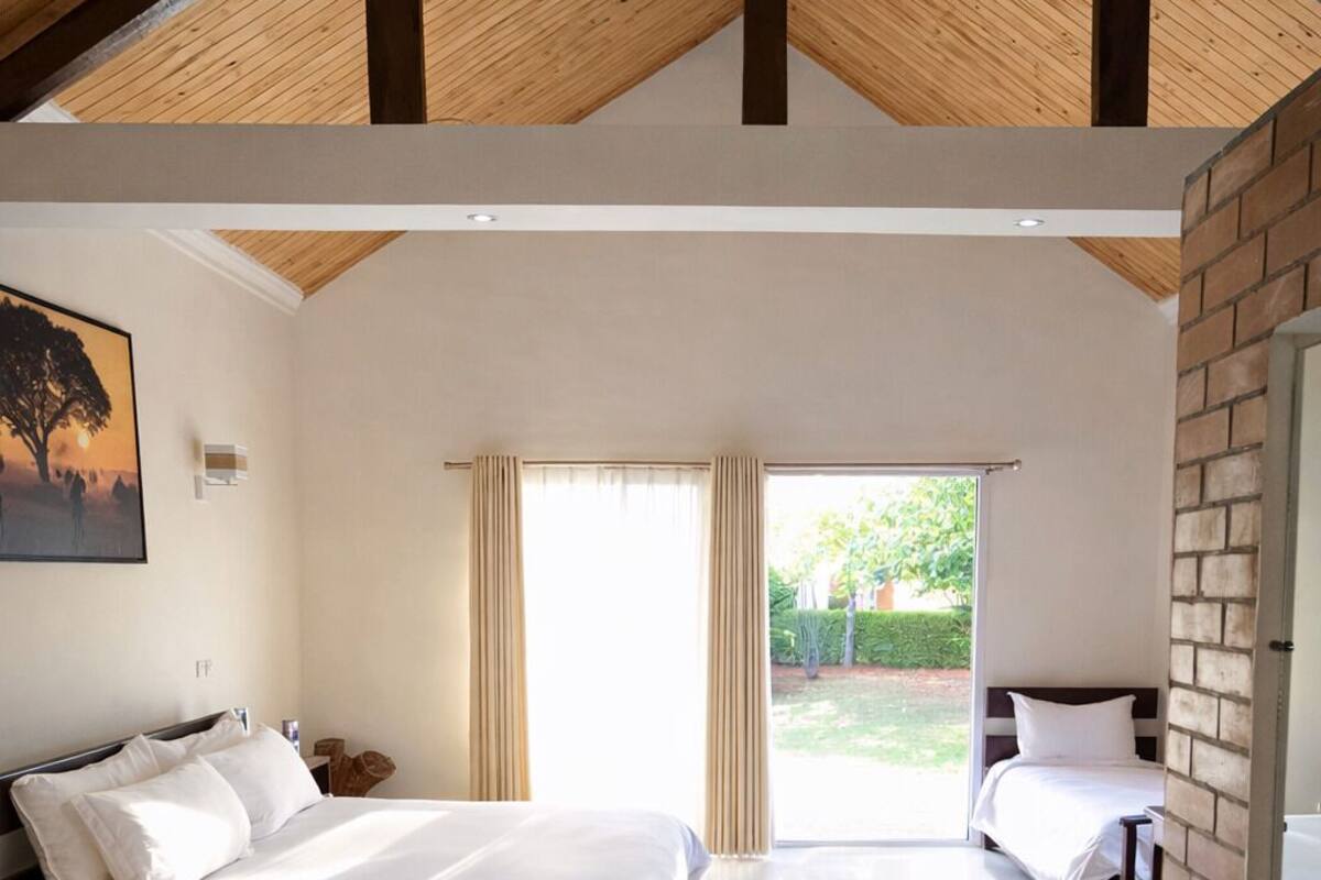 A bedroom with a large bed, a smaller bed, a wooden ceiling, and a view of the outdoors.