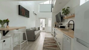 A modern kitchen with a dining area, a sofa, and a TV mounted on the wall.