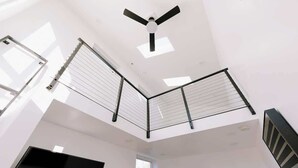 A modern interior with a ceiling fan, skylights, and a metal railing.