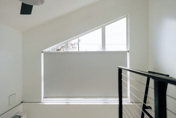 A room with a large window, a white wall, and a black railing.