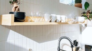 A modern kitchen with a white tiled backsplash, a wooden shelf with kitchenware, a window, and a cactus plant.