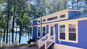 A two-story blue house with a front porch, a grill, and a view of a lake. - Waterview Family Style 2 Bed Cabin #8 (Charlotte)