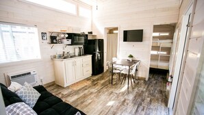 A compact kitchen with a microwave, stove, and sink, a dining area with a table and chairs, and a cozy seating area with a sofa and cushions. - Waterview Family Style 2 Bed Cabin #8 (Charlotte)