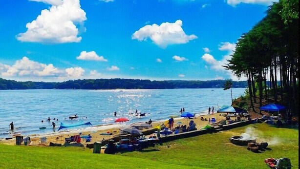 A beach scene with people swimming and sunbathing, tents, and a grassy area. - Waterview Family Style 2 Bed Cabin #8 (Charlotte)