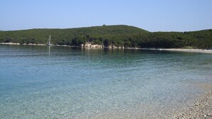 A calm lake with clear water, a small boat, and a forested hill in the background. - Villa Bacchus (Corfu)