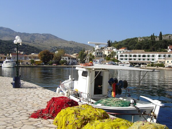 A harbor with boats, a cobblestone dock, and buildings in the background. - Villa Bacchus (Corfu)