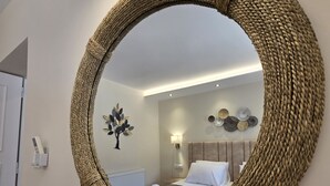 A room with a large woven mirror on the wall, a bed with white linens, a headboard, and a wall-mounted light fixture. - Villa Bacchus (Corfu)