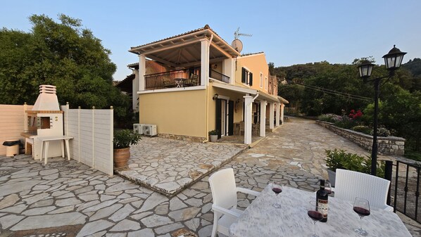A two-story house with a stone patio, outdoor seating, and a barbecue area. - Villa Bacchus (Corfu)
