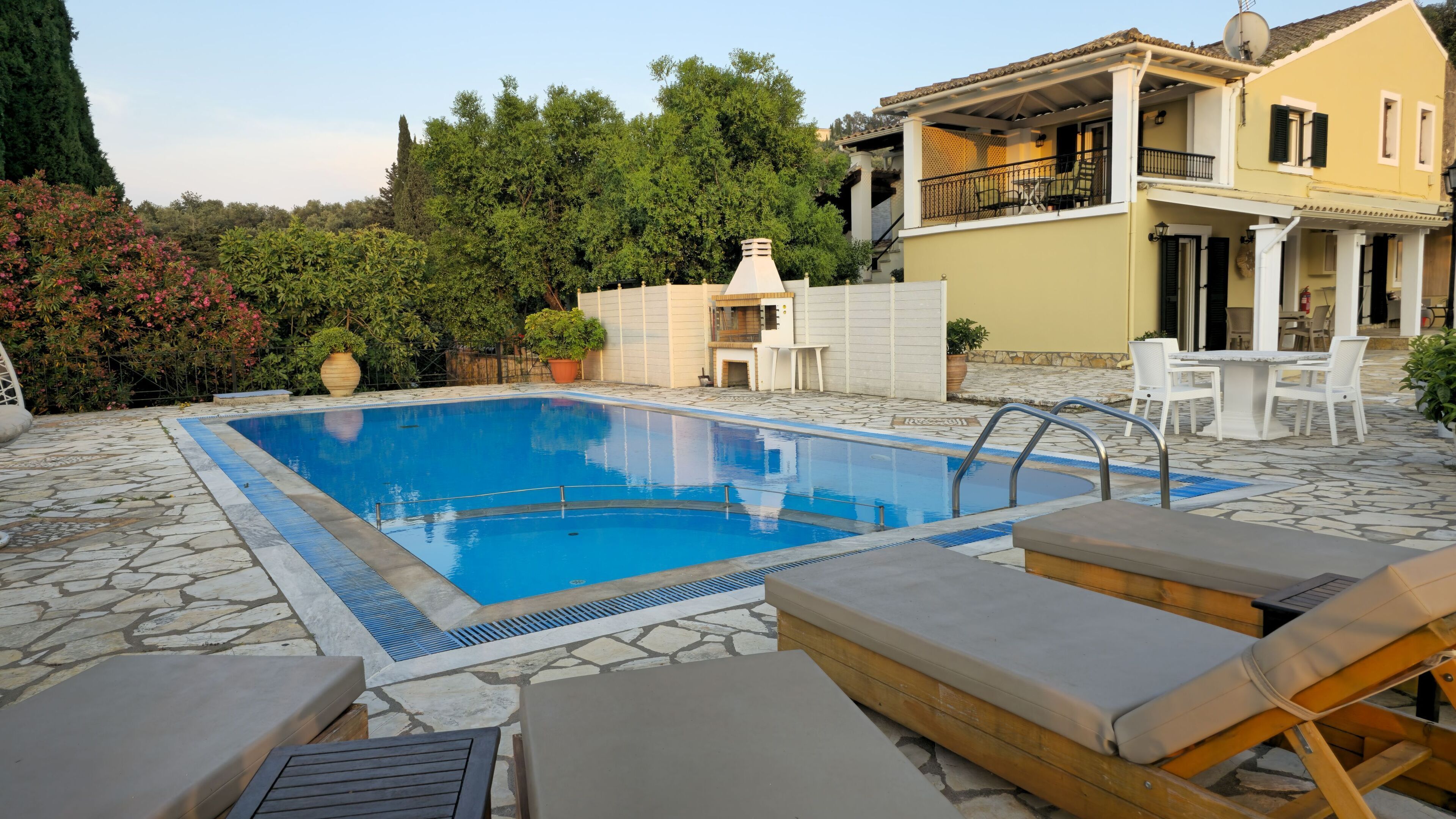 A swimming pool with lounge chairs, a stone patio, and a building with a balcony.