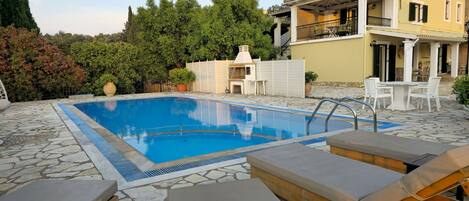 A swimming pool with lounge chairs, a stone patio, and a building with a balcony.