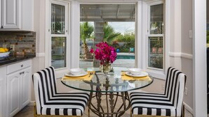A dining area with a glass table, two striped chairs, and a vase of pink flowers. - Wall Street Journal Featured-6 bath Lux Resort Home (Paradise Valley)