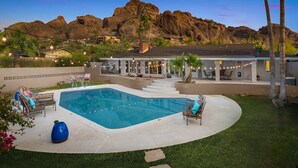 A pool area with a clear view of the surrounding landscape, including rocky hills and a house with outdoor seating. - Wall Street Journal Featured-6 bath Lux Resort Home (Paradise Valley)
