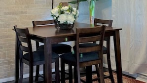 Un coin repas avec un mur en briques, un luminaire au plafond et une table avec des chaises. On peut voir une plante et un panier de fleurs sur la table.