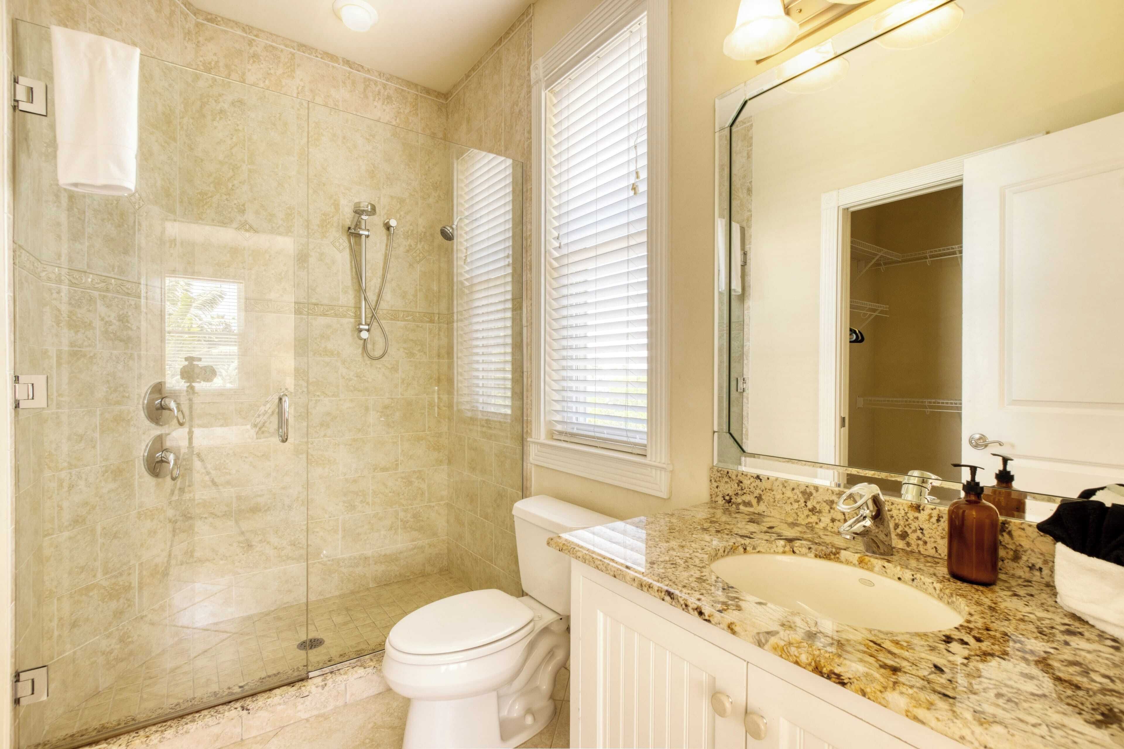 A bathroom with a glass-enclosed shower, a toilet, a sink with a granite countertop, and a large mirror.