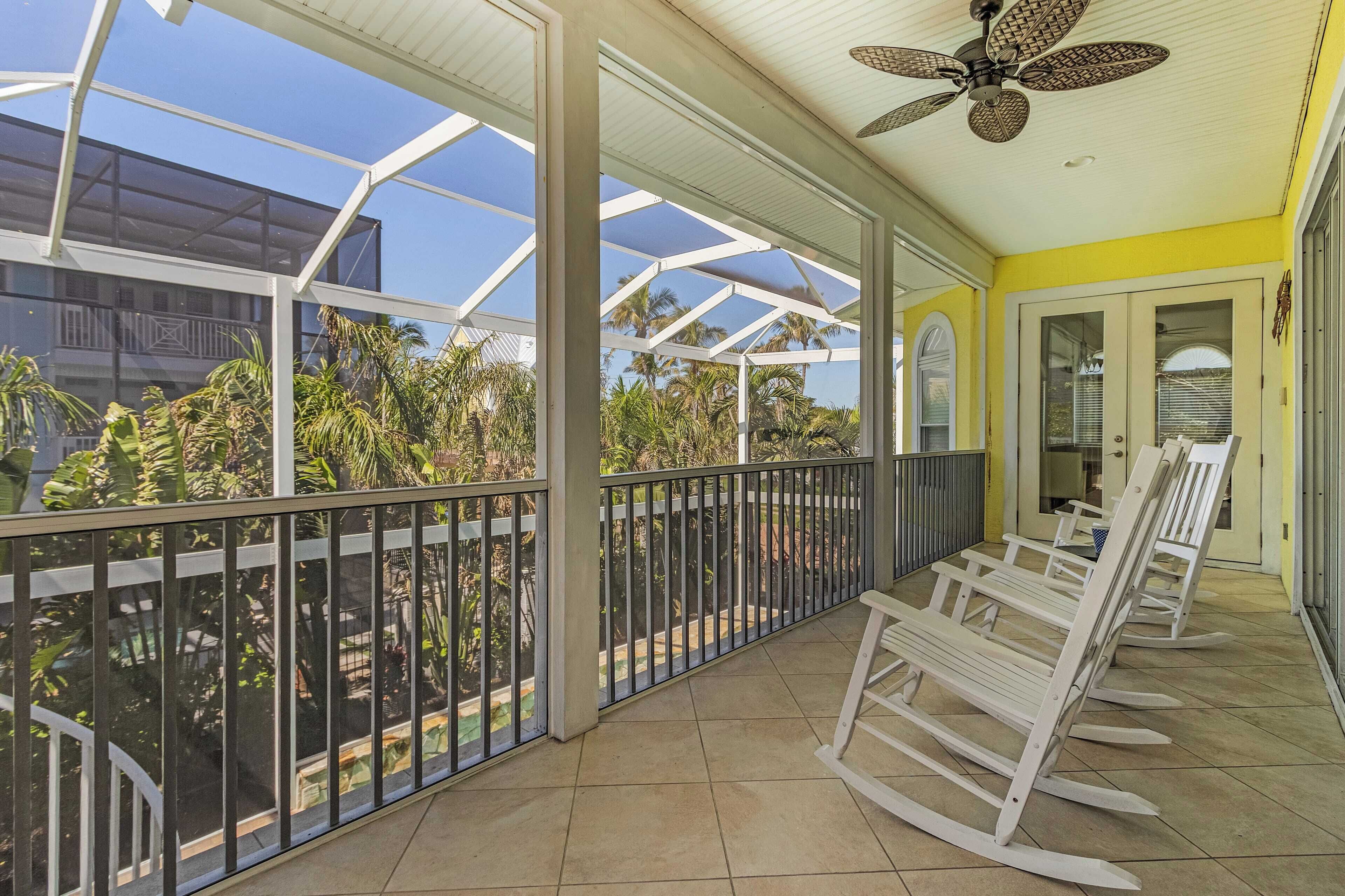 A covered balcony with a view of palm trees, a ceiling fan, and a yellow wall.