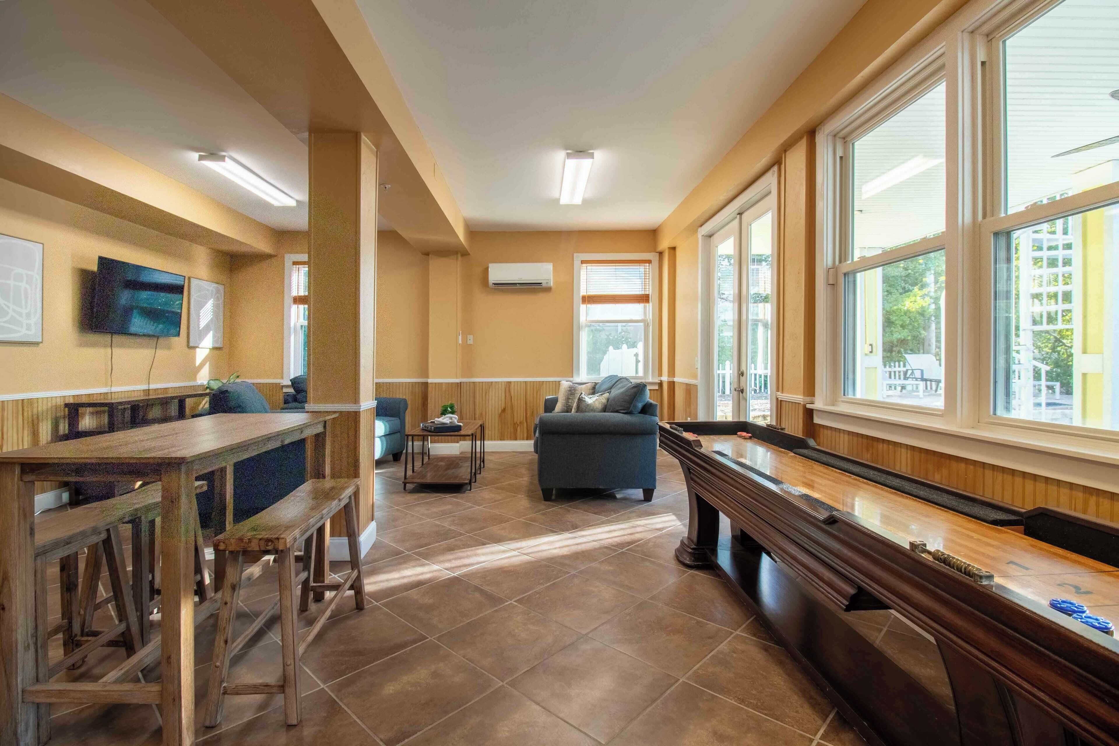 A spacious living area with a pool table, comfortable seating, and large windows offering a view of the outside.