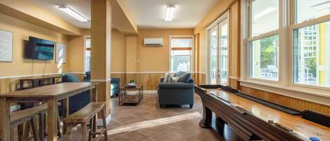 A spacious living area with a pool table, comfortable seating, and large windows offering a view of the outside.