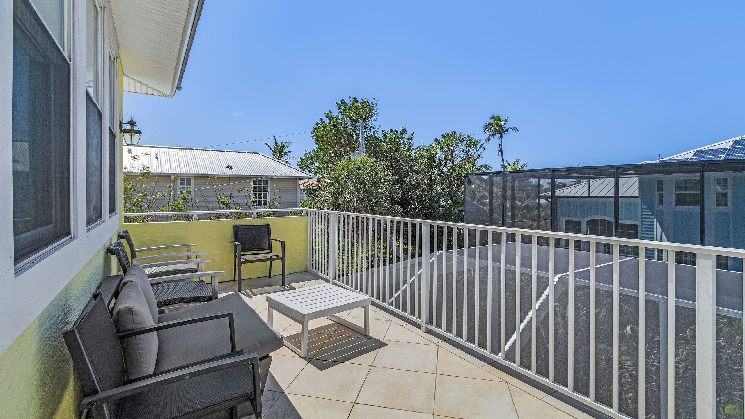A balcony with outdoor furniture, a white railing, and a view of the surrounding area including trees and buildings.