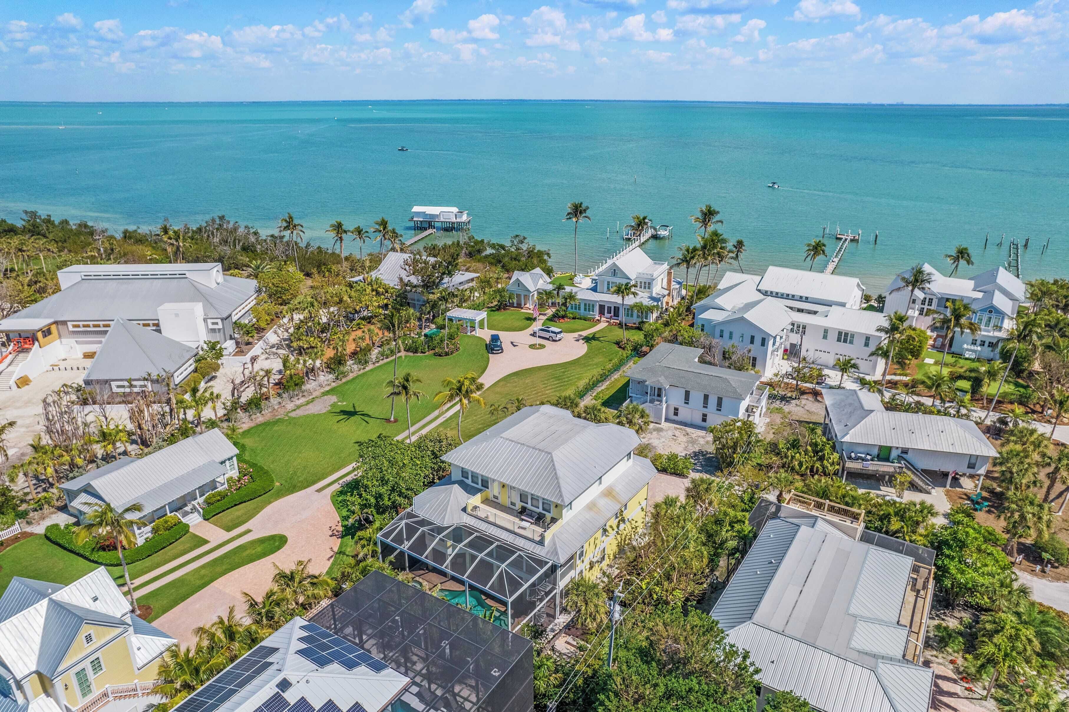 Una vista aerea di una zona residenziale costiera con diverse case, una spiaggia e un molo che si protende nell'acqua.