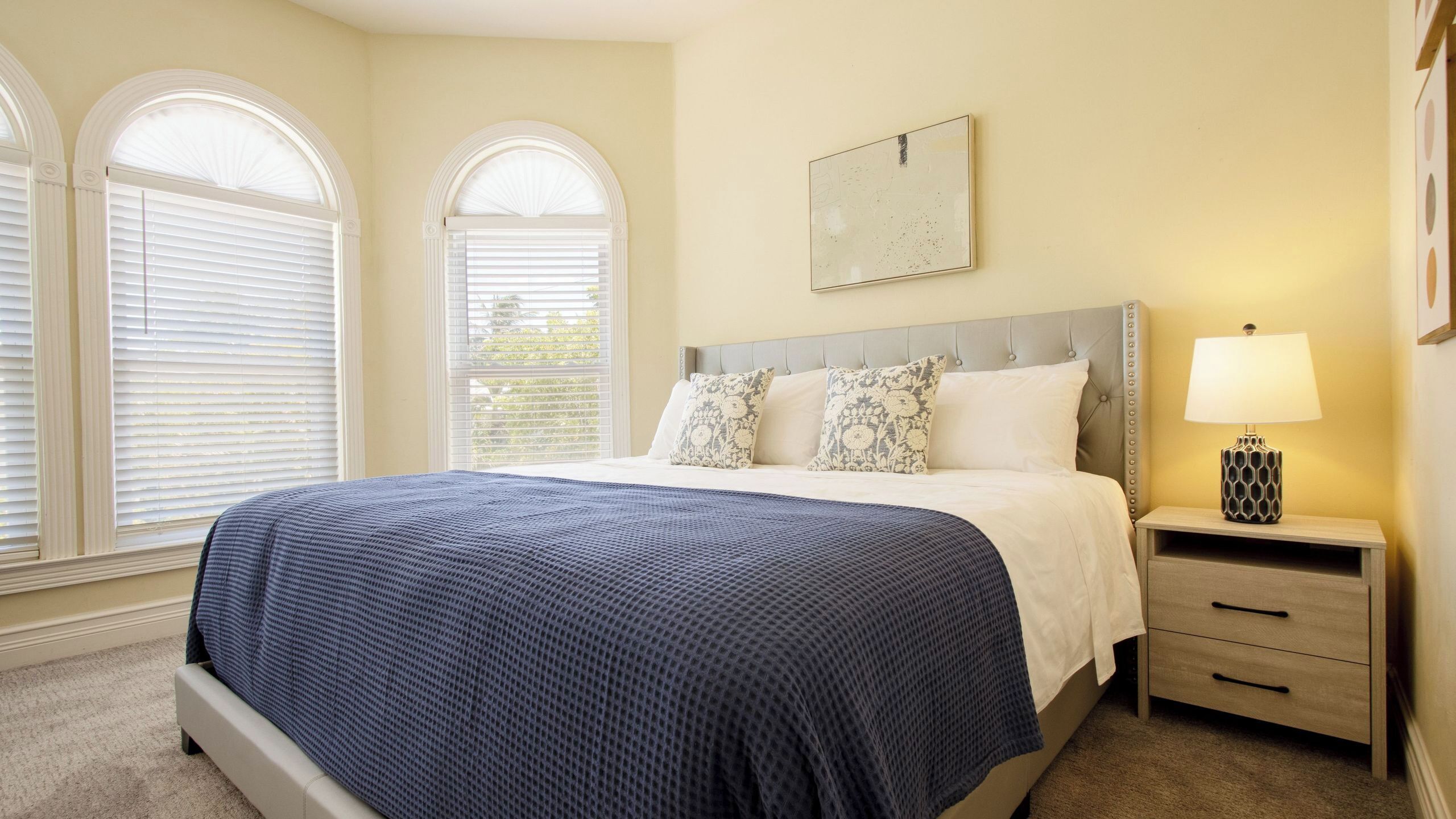 A bedroom with a large bed, two bedside tables, a nightstand, and a wall-mounted lamp.