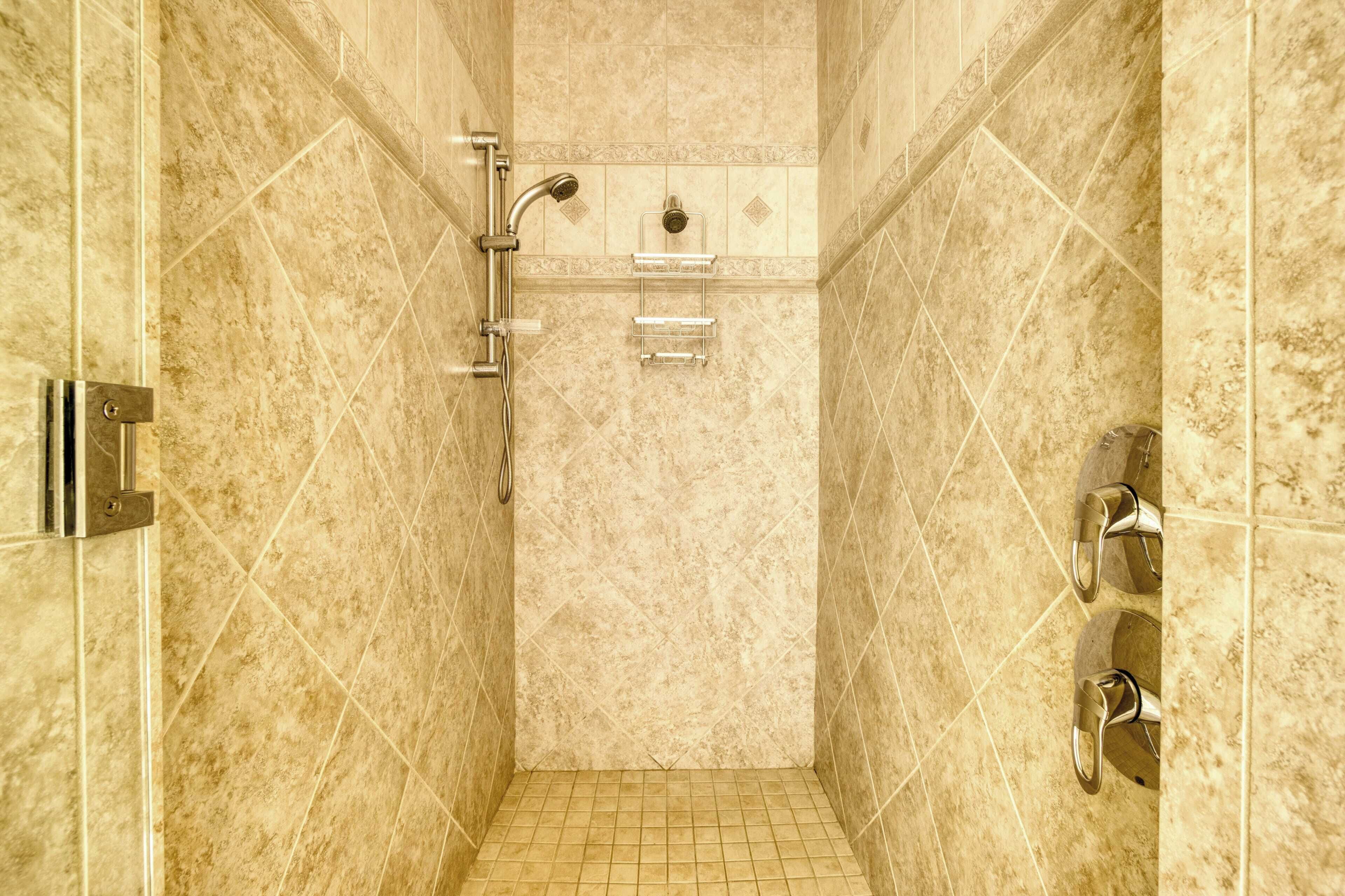 Zona de ducha con azulejos, ducha de mano, grifo empotrado y toallero.