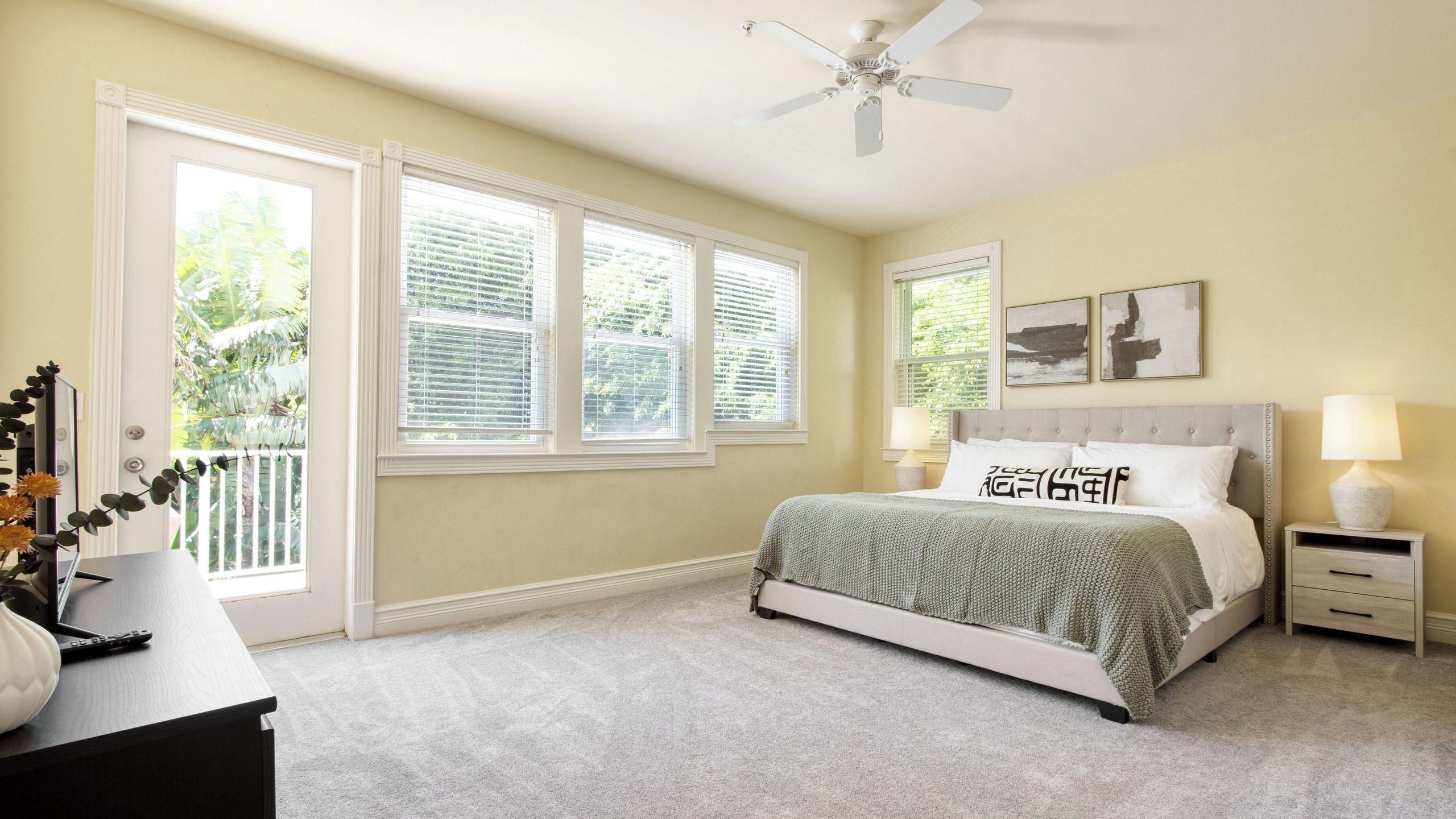 A bedroom with a bed, bedside tables, a ceiling fan, and large windows.