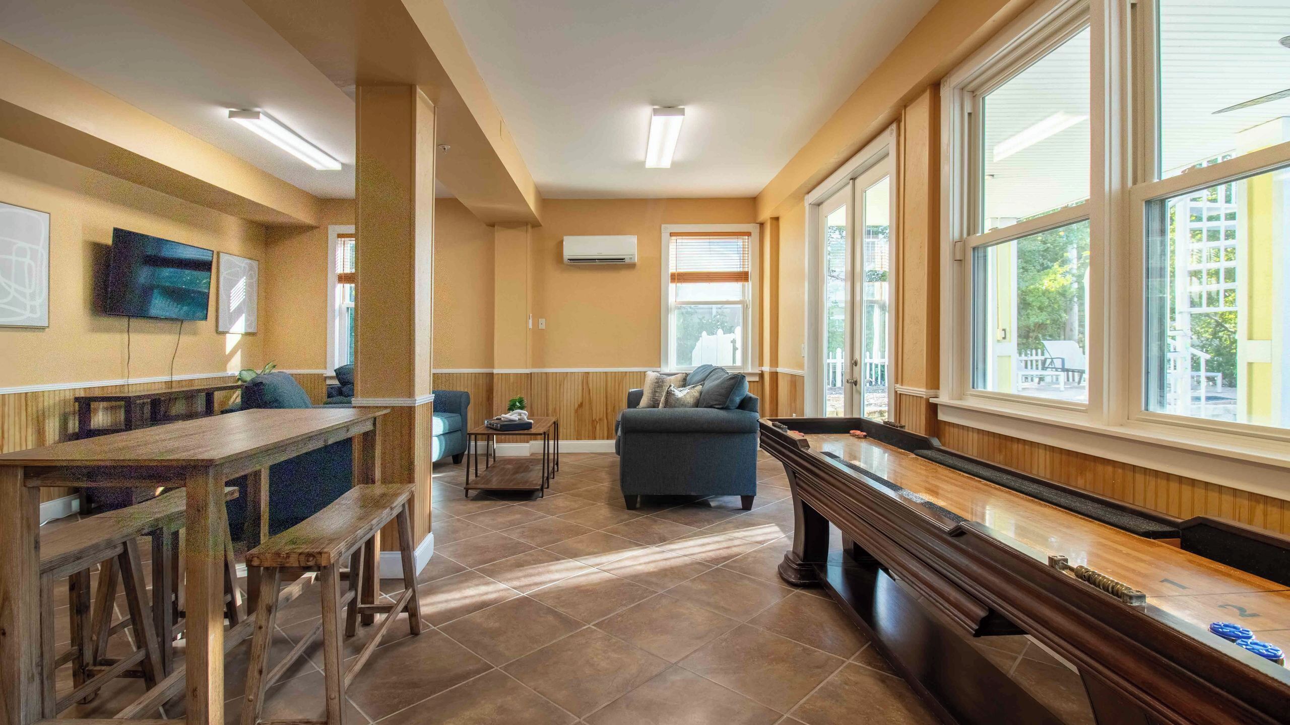 A spacious living room with a pool table, comfortable seating, and large windows.