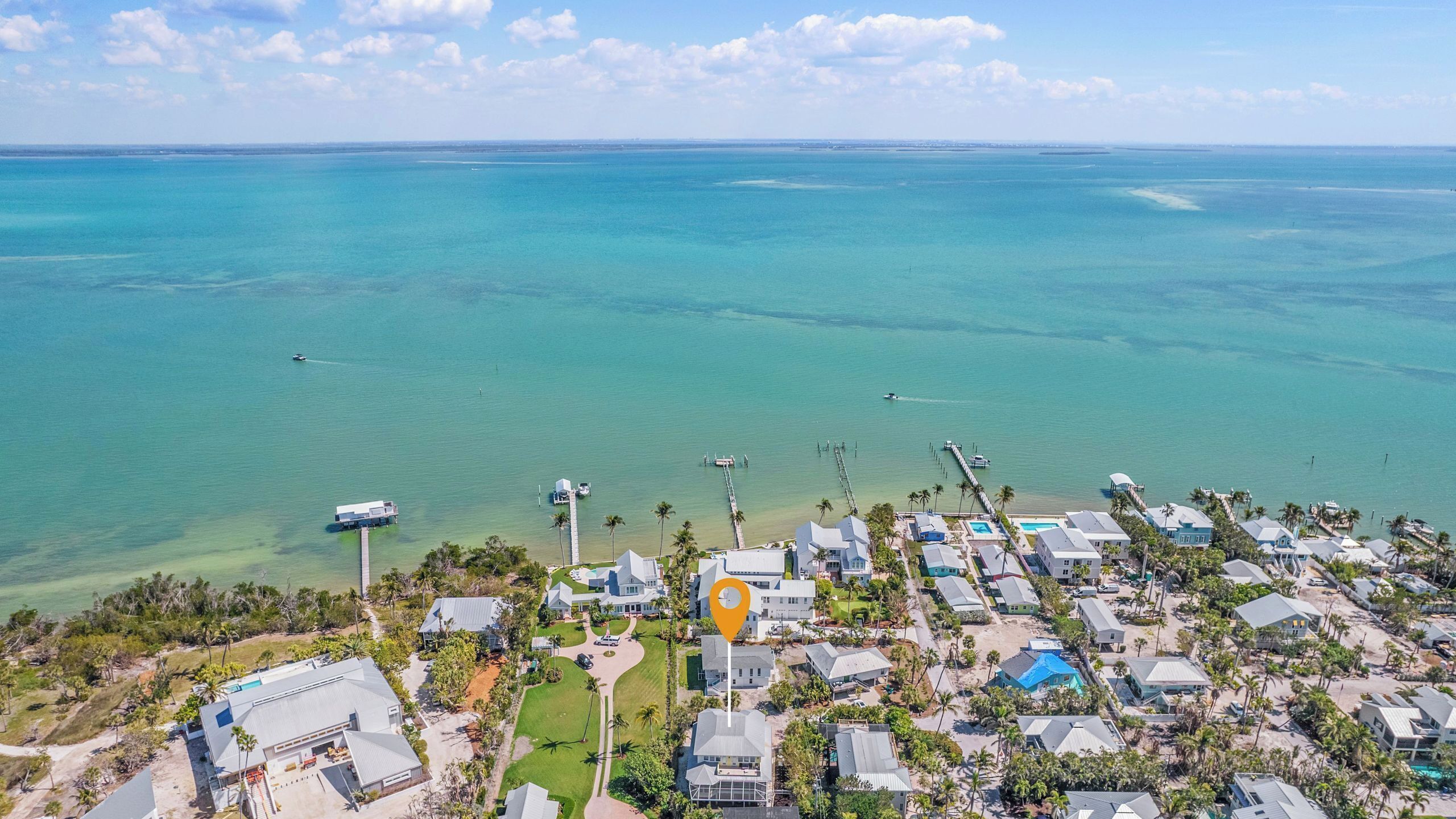 An aerial view of a coastal residential area with houses, a dock, and a clear view of the ocean.