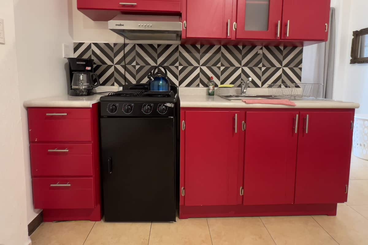 Uma cozinha compacta com armários vermelhos, fogão preto e máquina de café.