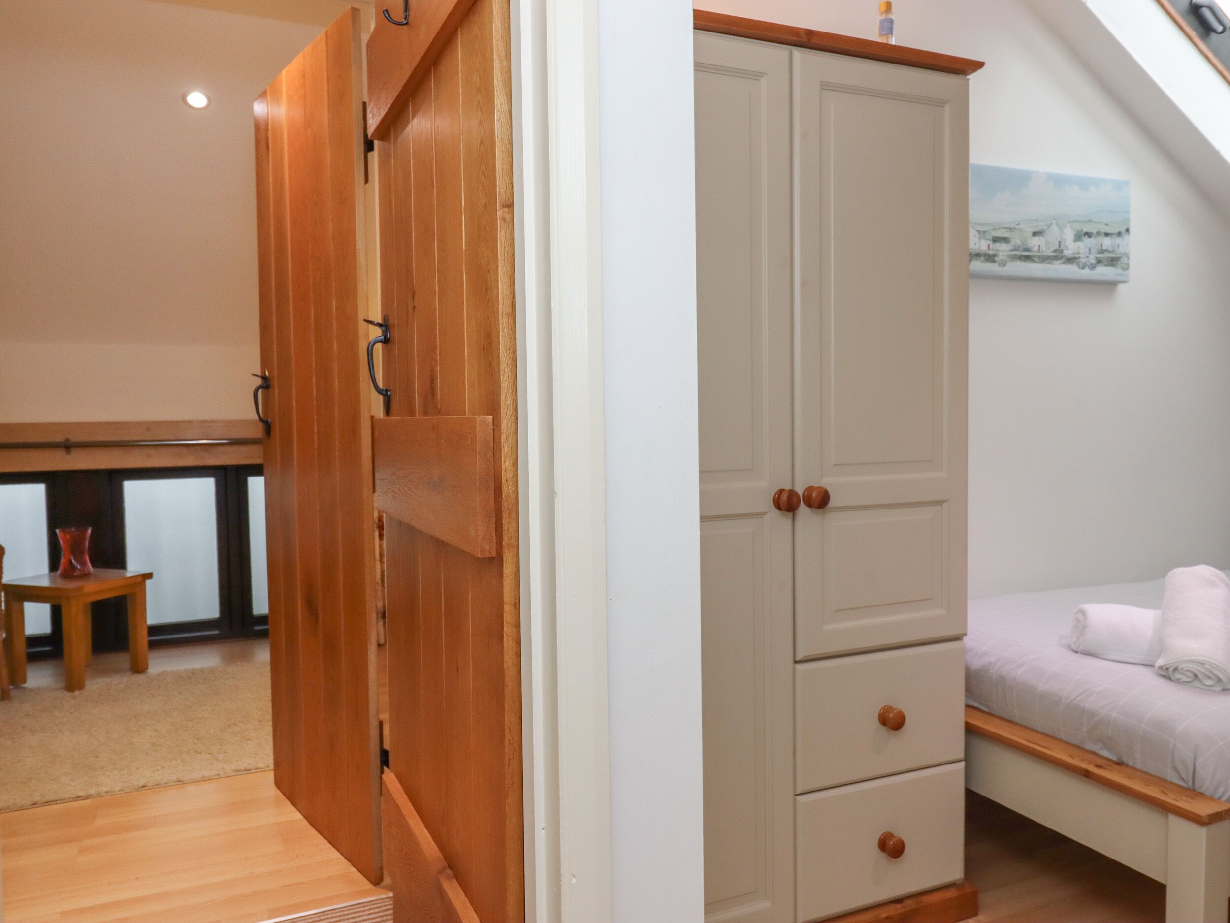 Une chambre avec une armoire en bois, un lit avec une literie blanche et un tableau accroché au mur.