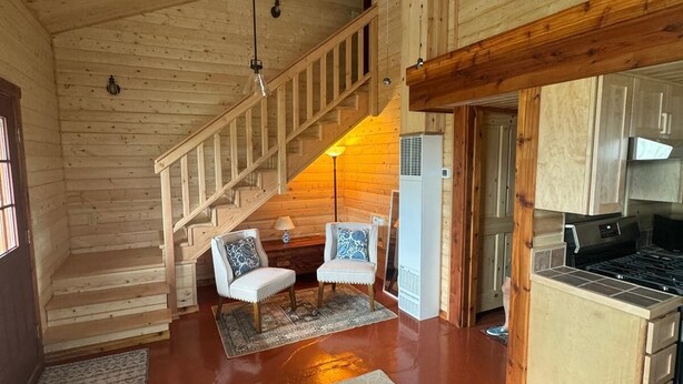 Een ruime woonkamer met een houten trap, een keuken en een eethoek met twee stoelen.