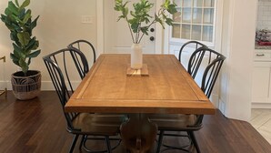 Una sala da pranzo con un tavolo di legno, sedie nere, un vaso bianco con piante e un lampadario.