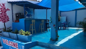 A blue outdoor seating area with a 'WELCOME Casa Santorini' sign, steps leading up to a bar area, and outdoor furniture. - HOSTAL CASA SANTORINI (Cartagena)
